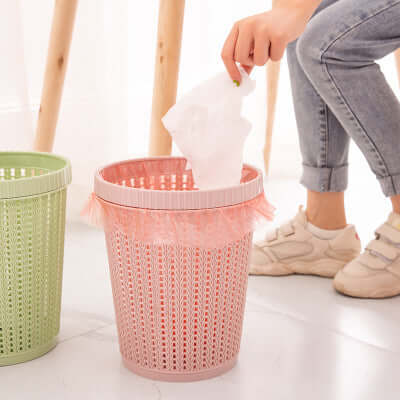 A person using a portable garbage bag with box in a pink, stylish wastebasket for easy disposal.