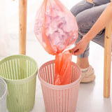 Portable garbage bag with box being used to remove trash from a pink bin, featuring orange trash bag.