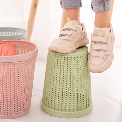 Person standing on a green portable garbage bag with box while next to pink and green garbage bins.