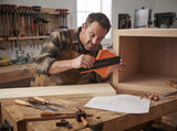 A woodworker using contour gauge to scribe cabinet edge in workshop